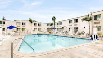 A swimming pool with lounge chairs and umbrellas, surrounded by multi-story buildings with balconies.