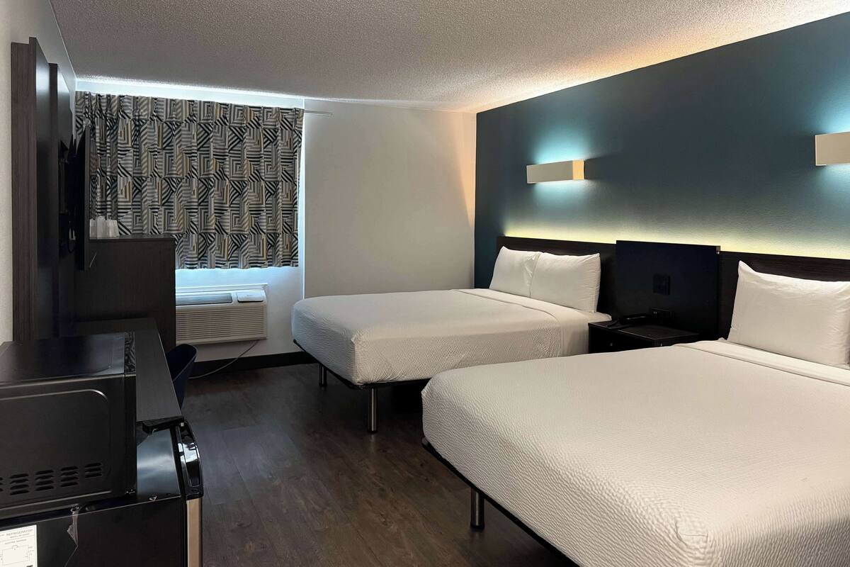 A hotel room with two beds, a desk, and a window with patterned curtains.