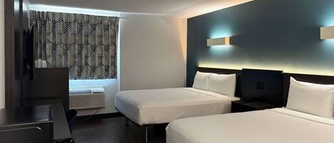 Habitación de hotel con dos camas, un escritorio y una ventana con cortinas estampadas.