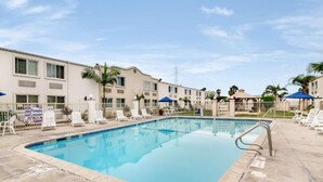 A swimming pool with lounge chairs and umbrellas, surrounded by buildings with a uniform architectural style.