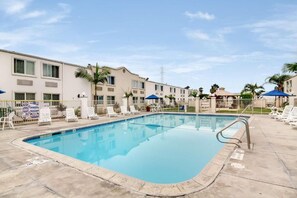 A swimming pool with lounge chairs and umbrellas, surrounded by buildings with a uniform architectural style.