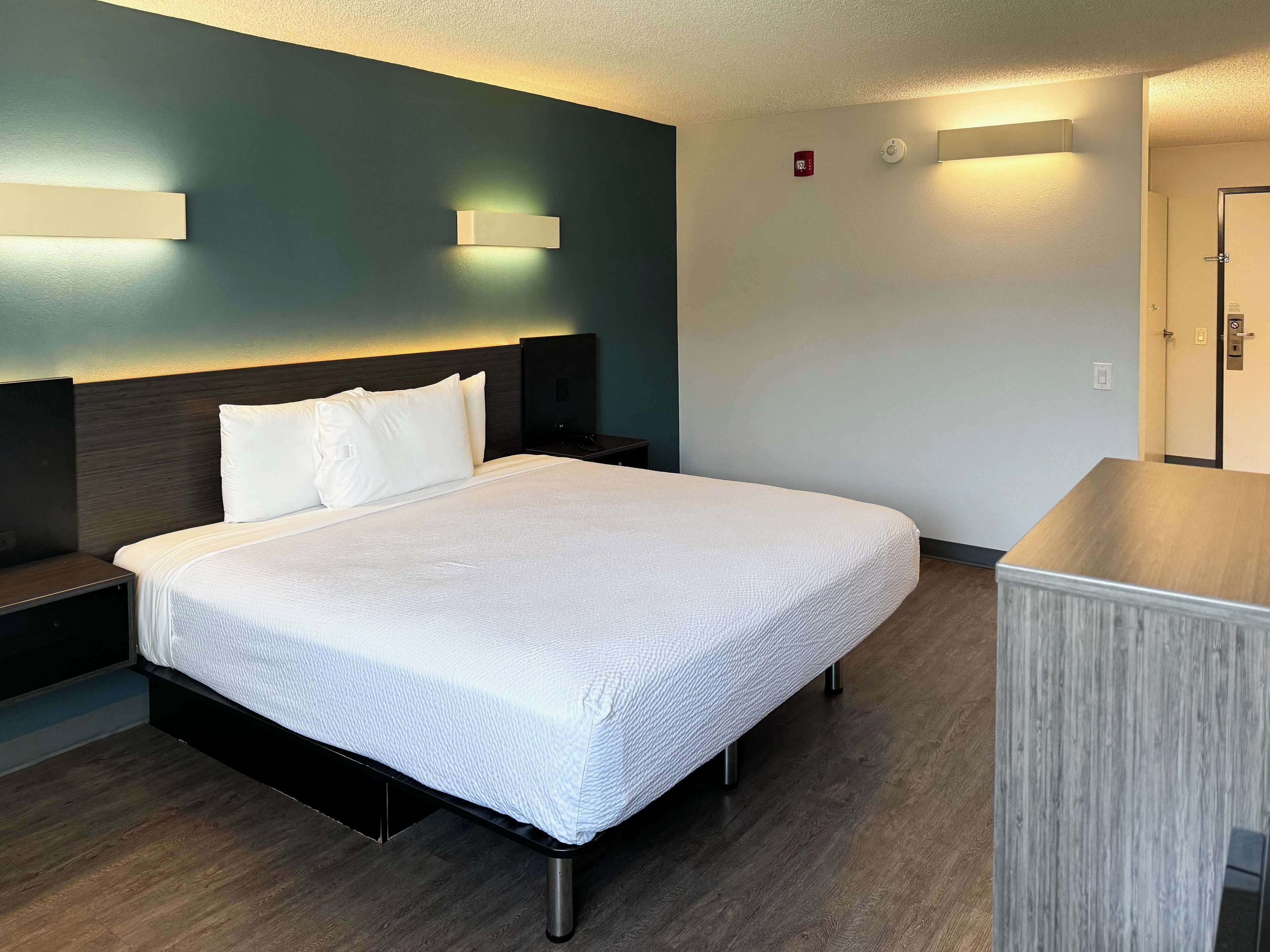 A hotel room with a bed, bedside tables, a desk, and a wardrobe.