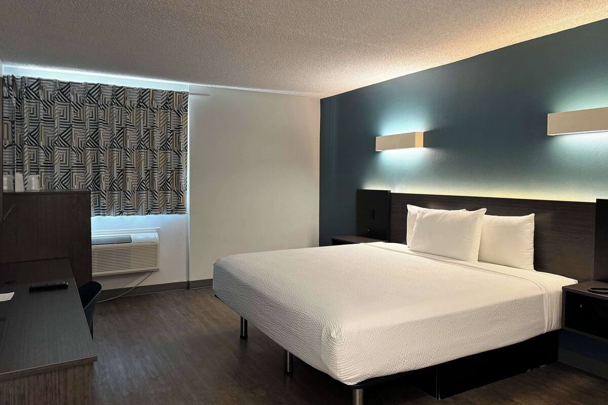A hotel room with a large bed, a desk, and a patterned curtain.