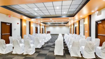 Un salón de conferencias con filas de sillas cubiertas de blanco, una alfombra a cuadros e iluminación empotrada en el techo.