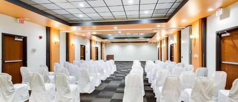 A conference room with rows of chairs covered in white, a checkered carpet, and a ceiling with recessed lighting.