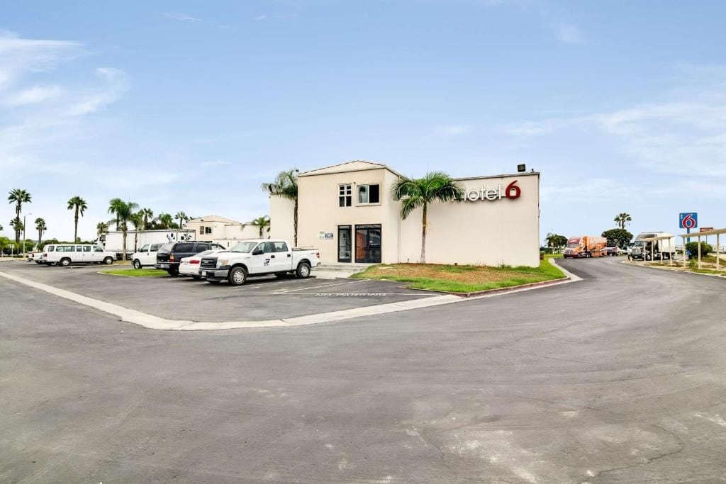 A hotel with a parking lot, a building with a sign, and palm trees in the background.