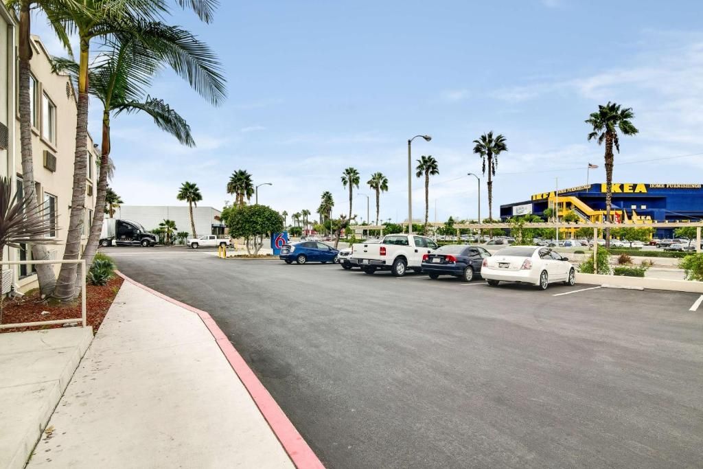 A parking lot with several cars, a building with a blue and yellow sign, and palm trees.
