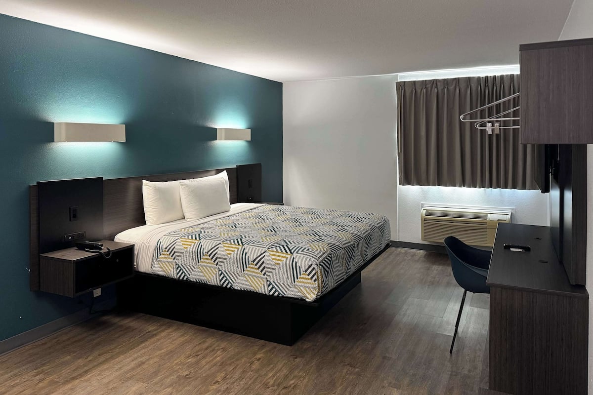 A modern hotel room with a bed, bedside table, and a desk with a chair.