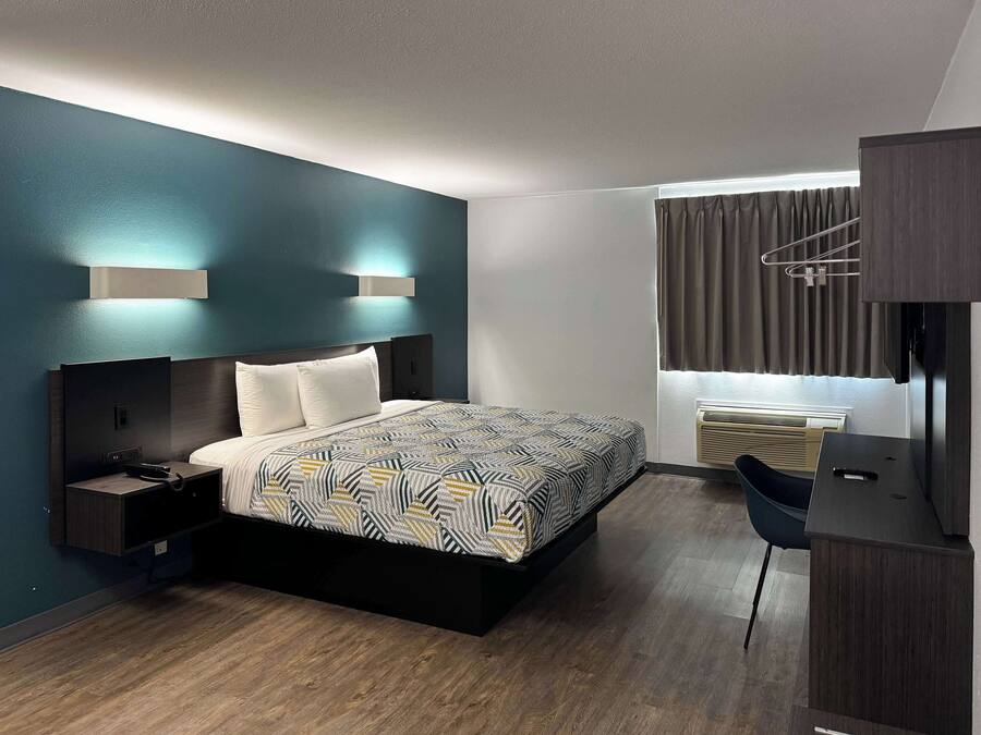 A modern hotel room with a bed, bedside table, and a desk with a chair.