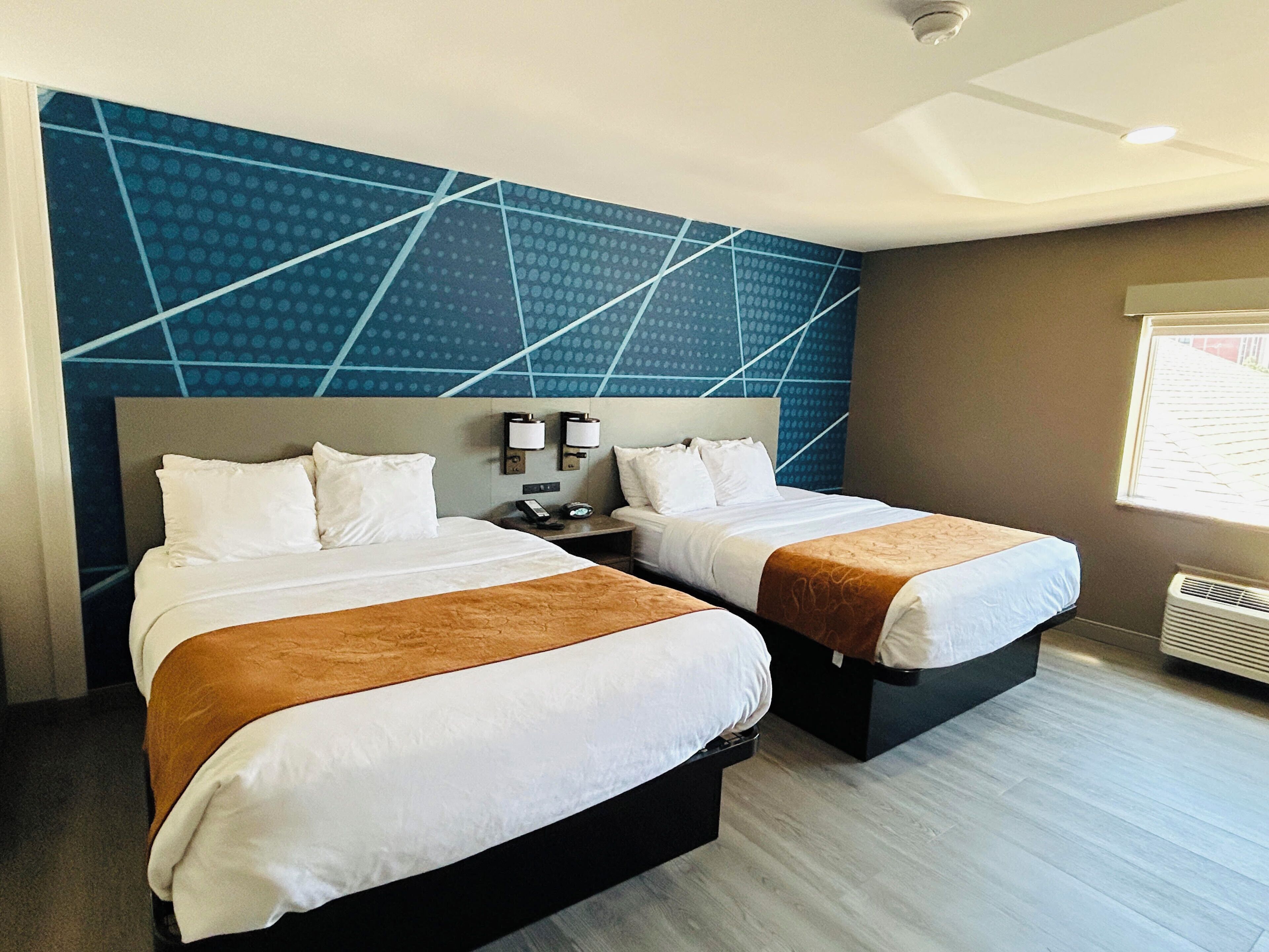 A hotel room with two beds, a modern blue wall design, and a window with blinds.