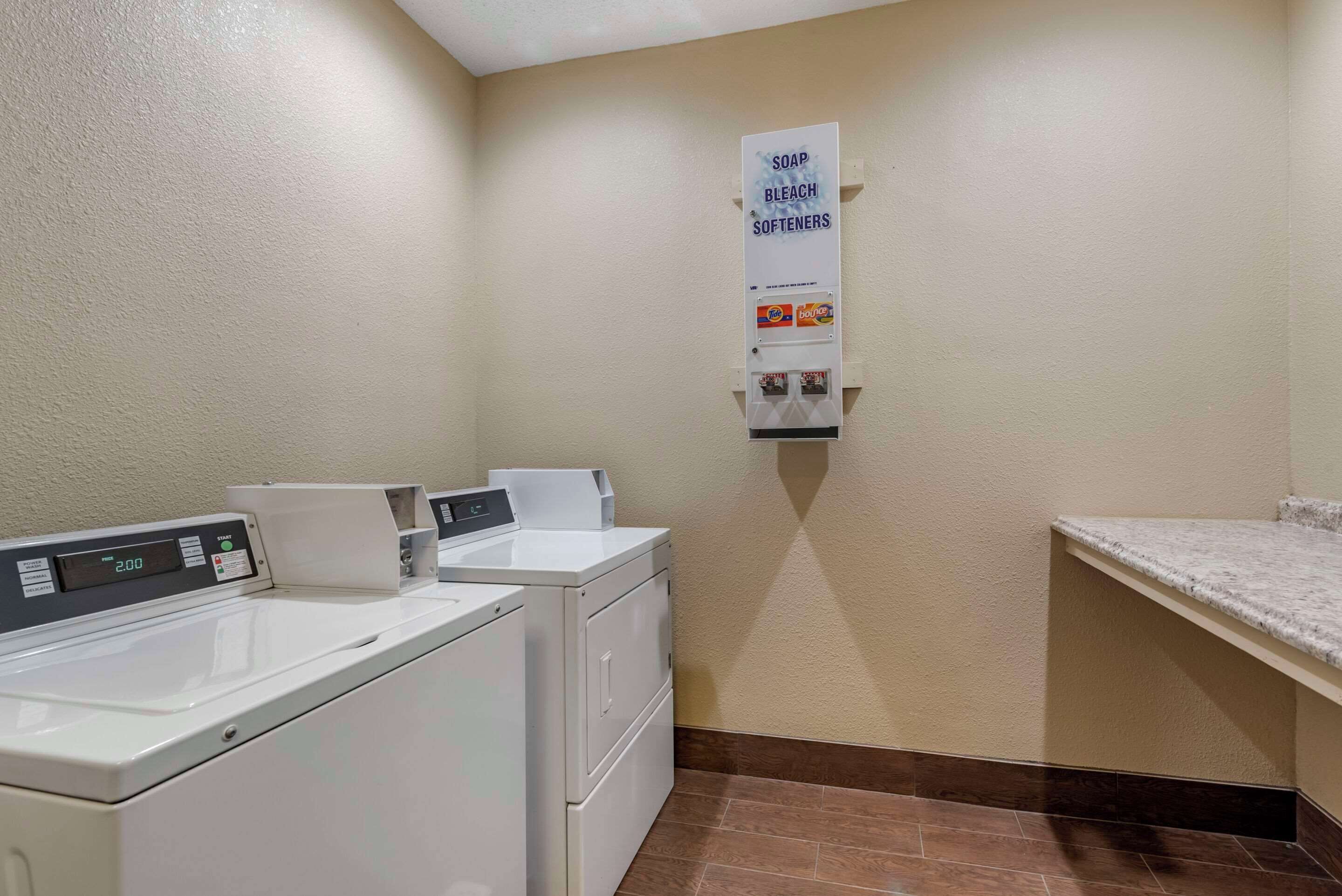 A laundry area with two washing machines, a soap and bleach dispenser, and a countertop.