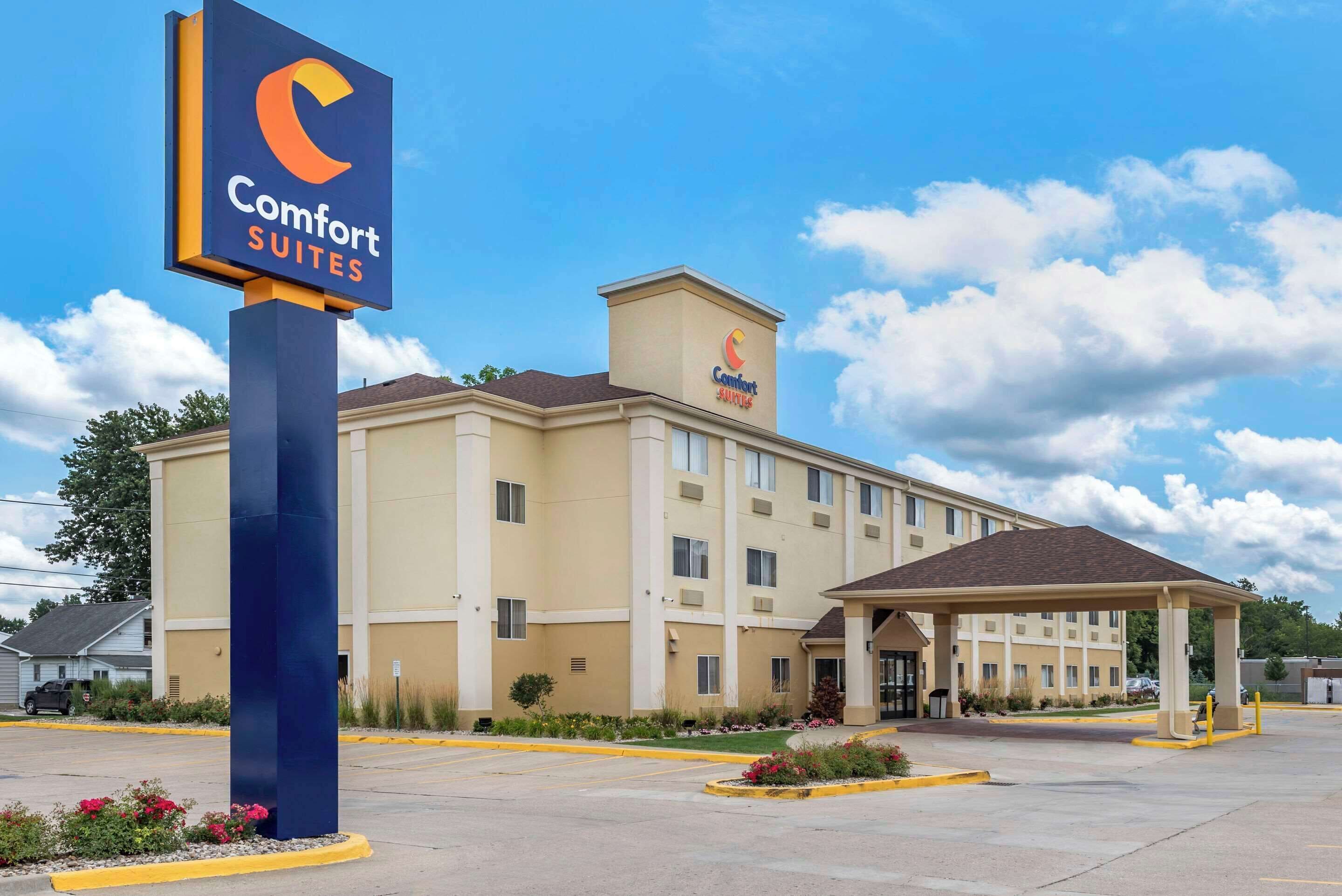 A Comfort Suites hotel with a large sign, a parking lot, and a covered parking area.