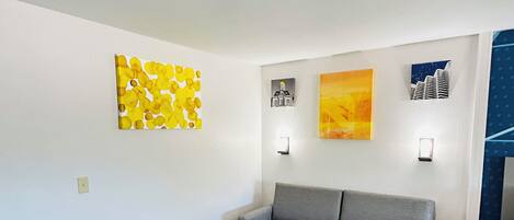 A modern living room with a grey sofa, a yellow coffee table, and three artworks on the walls.