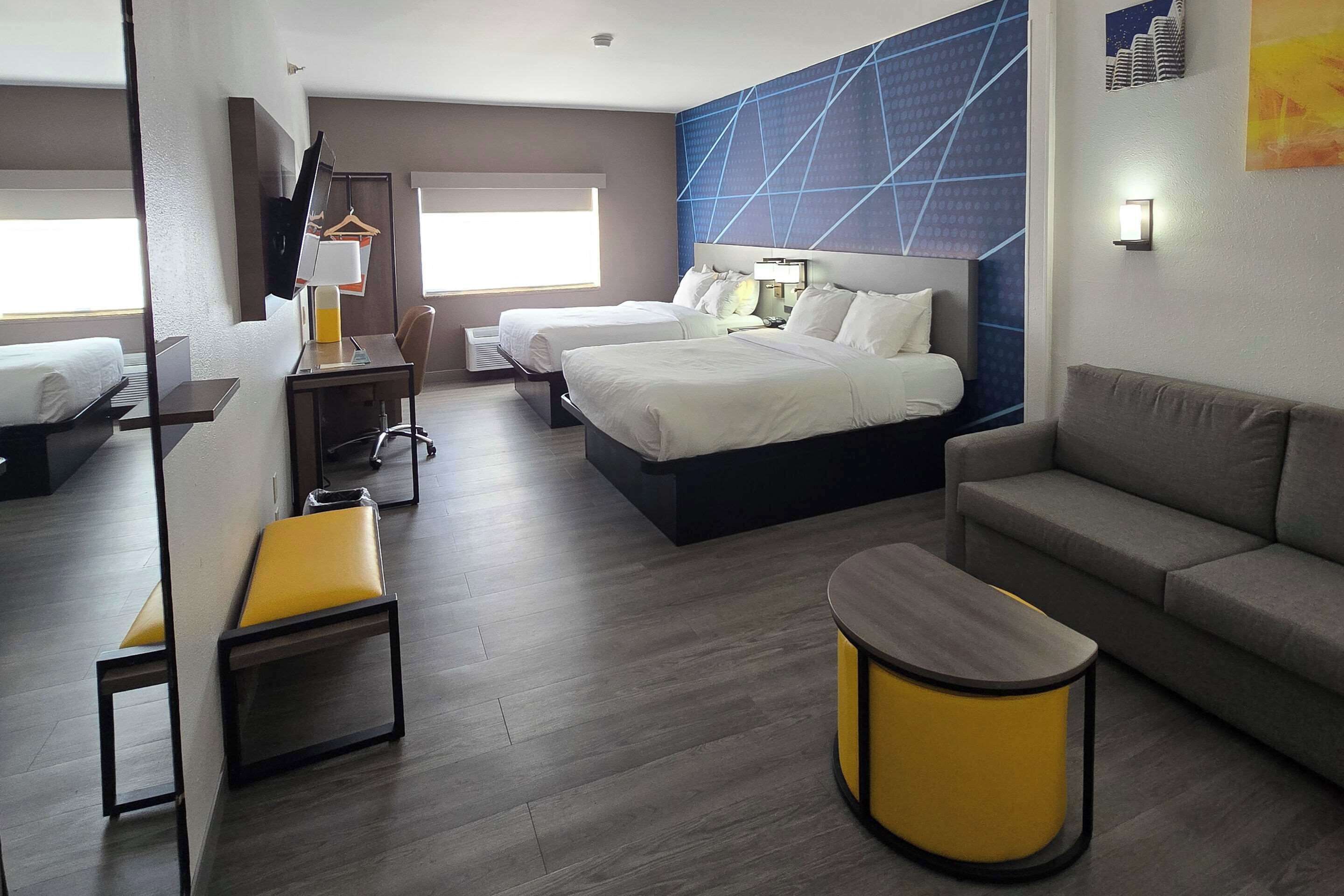 Une chambre d’hôtel avec deux lits, un canapé, un bureau avec une chaise, une petite table et un banc.