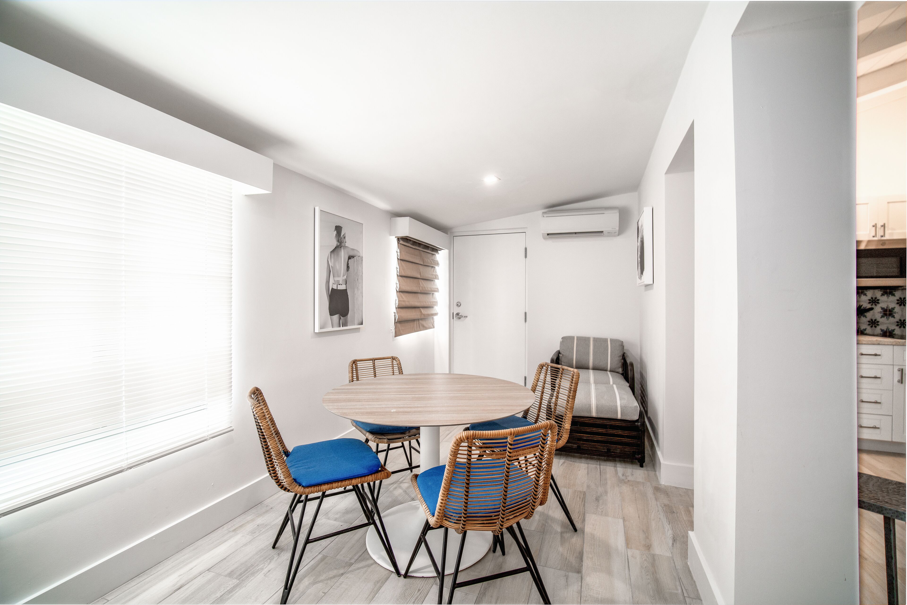 A compact living space with a round dining table, four wicker chairs with blue cushions, a sofa, and a small kitchenette.