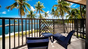 A balcony with two blue lounge chairs, a wooden ceiling, and a view of the ocean and palm trees. - Chesapeake Beach Resort (Islamorada)