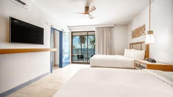 A hotel room with a large bed, a flat-screen TV, a ceiling fan, and a balcony with a view of palm trees.