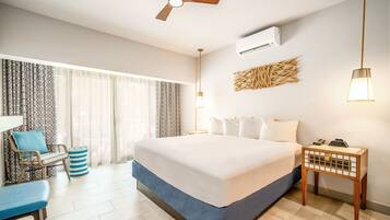 A hotel room with a large bed, a desk with a chair, a ceiling fan, and an air conditioning unit.