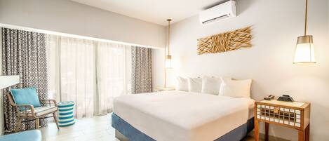 A hotel room with a large bed, a desk with a chair, a ceiling fan, and an air conditioning unit.