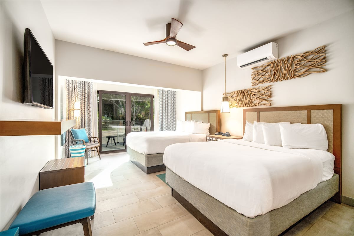 A hotel room with two beds, a desk, a chair, a TV, and a ceiling fan.