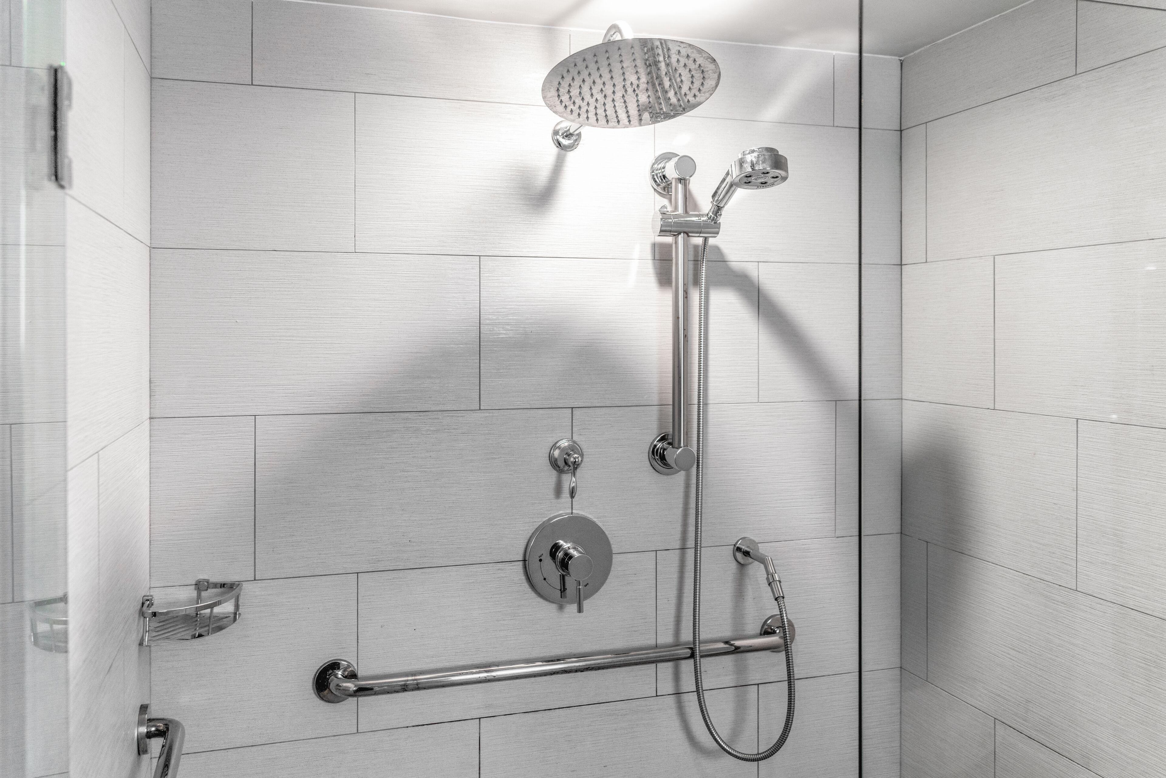 Une douche moderne dotée d’un pommeau de douche à main, d’un robinet mural et d’un autre pommeau de douche à main.