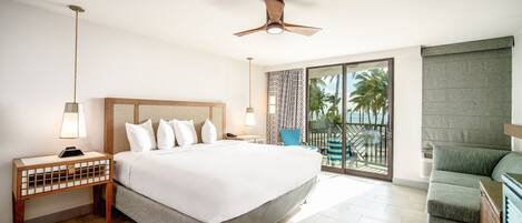 A hotel room with a large bed, a ceiling fan, a nightstand with a lamp, and a view of the outdoors through a sliding glass door.