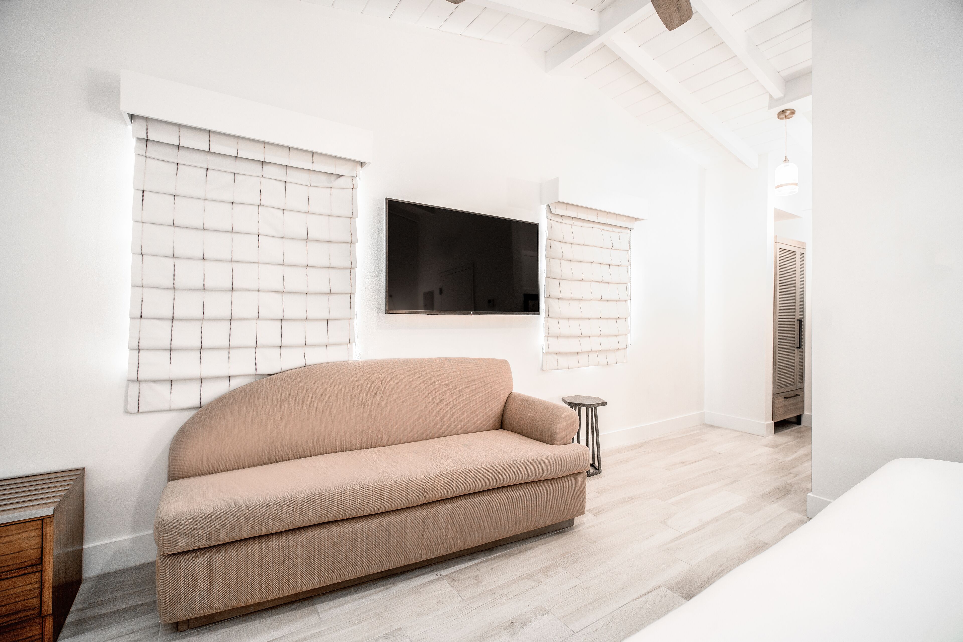 Una sala de estar moderna con un sofá color beige, un televisor de pantalla plana montado en la pared y una pequeña mesa auxiliar.