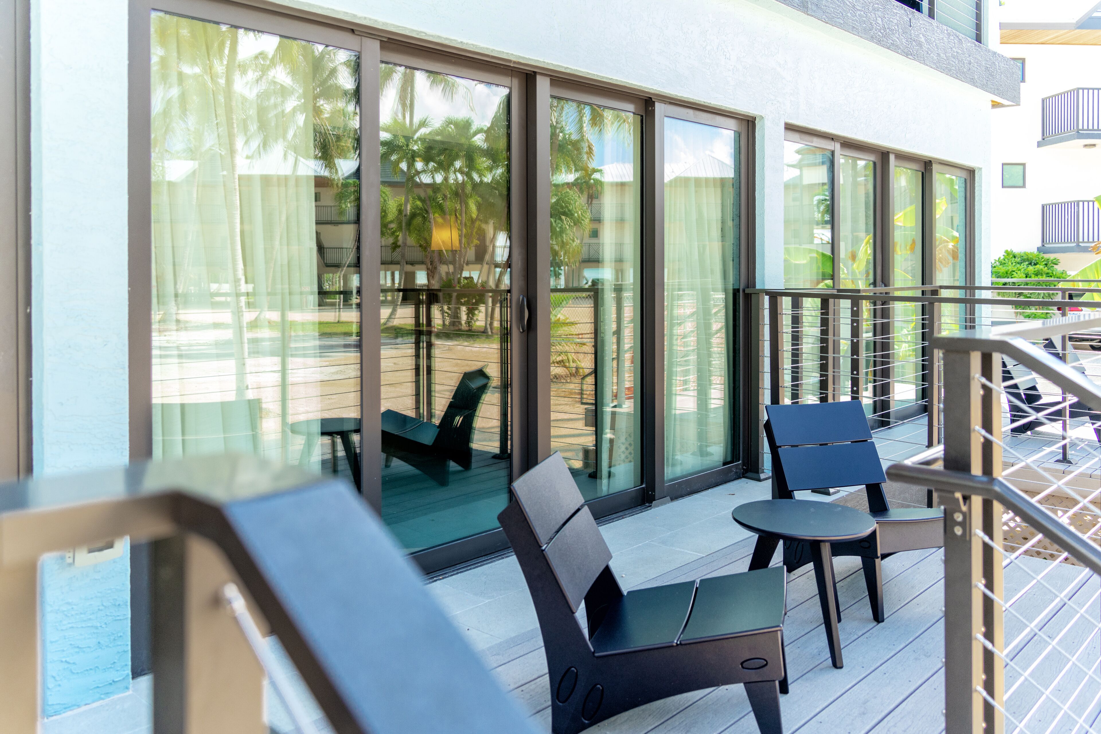 A balcony with a glass door leading to a pool area, furnished with chairs and a table.