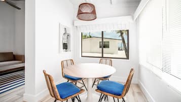 Un comedor con una mesa redonda y cuatro sillas de mimbre, un ventilador de techo y una ventana con persianas.