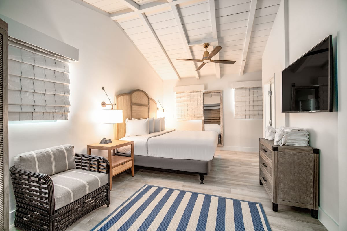 A bedroom with a bed, a sofa, a dresser, a TV, and a ceiling fan.