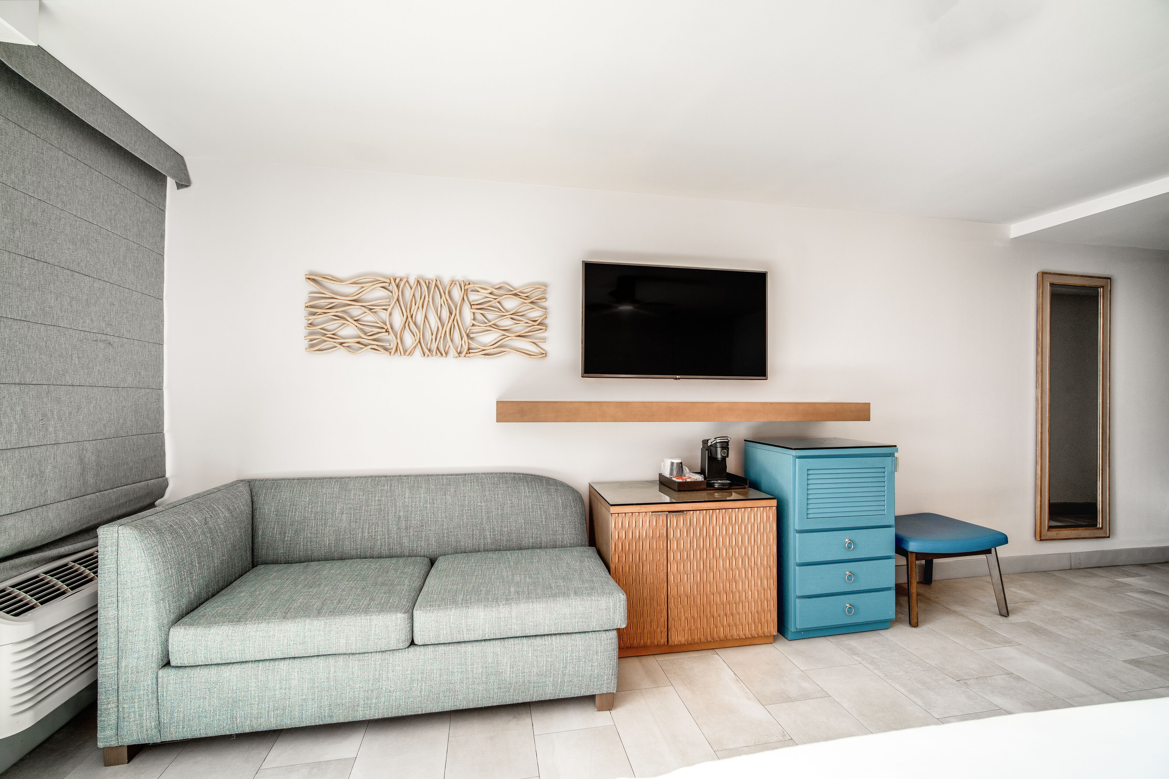 Ein modernes Wohnzimmer mit einem grauen Sofa, einem kleinen Holztisch, einem blauen Sessel, einem an der Wand montierten Fernseher und einer eingebauten Garderobe.