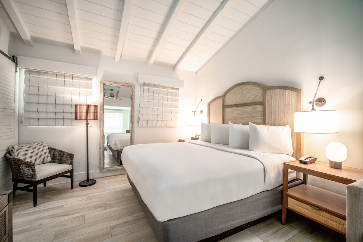 A neatly arranged hotel room with a large bed, a bedside table with a lamp, a chair, and a mirror.
