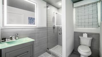 A modern bathroom with a glass shower enclosure, a white toilet, and a vanity with a glass countertop.