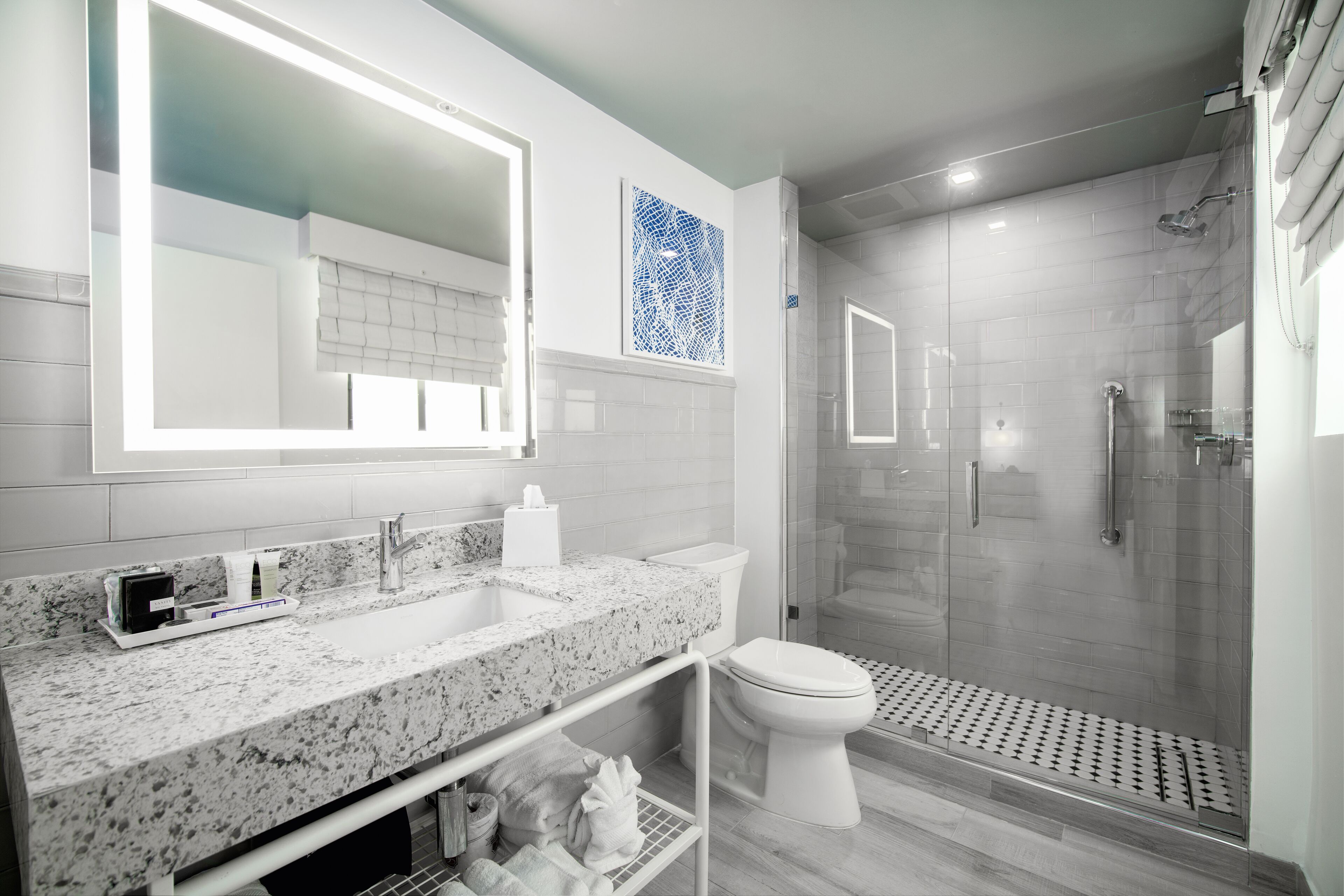 Un baño moderno con encimera de granito, inodoro blanco, ducha con mampara de vidrio y un espejo grande.