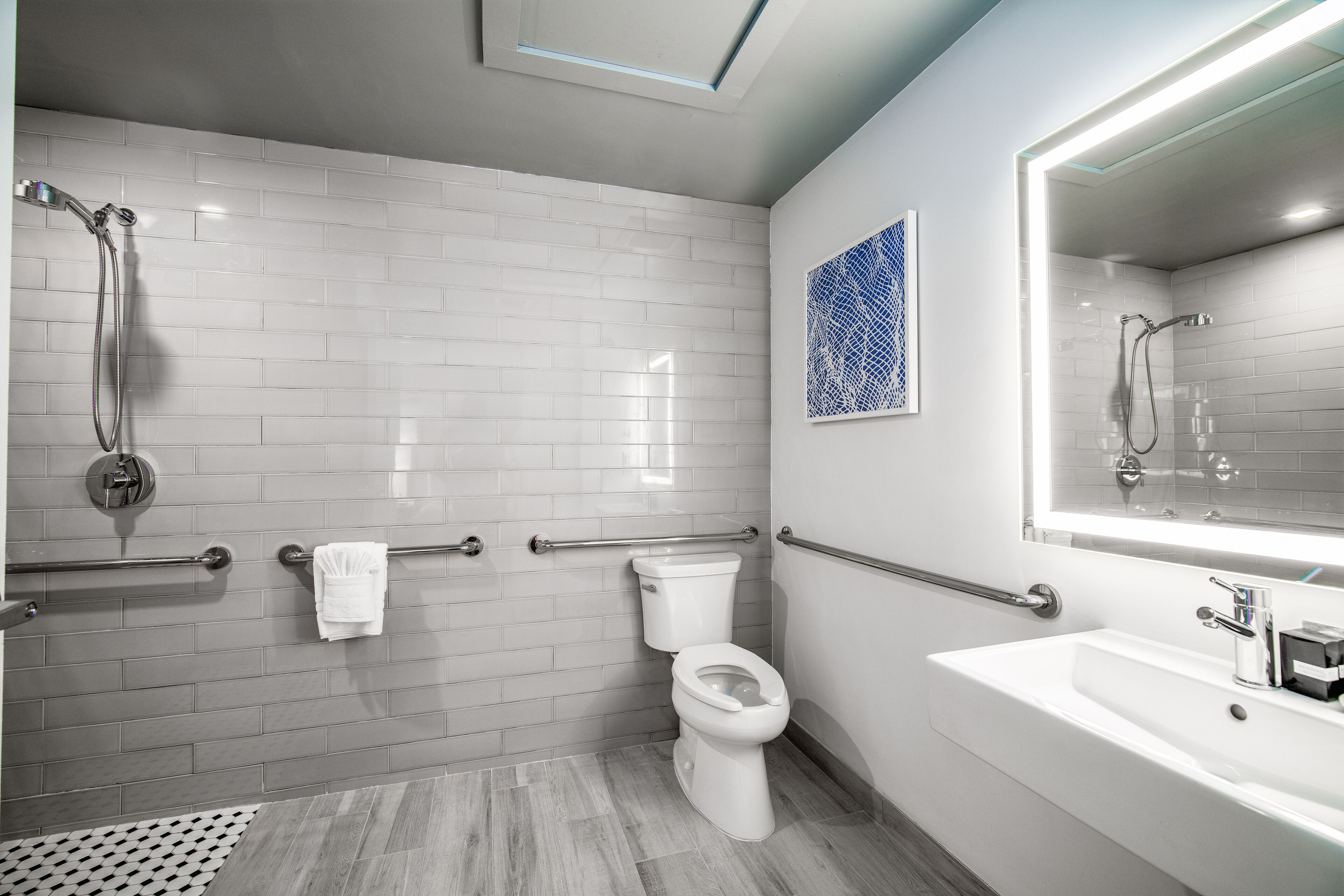 A modern bathroom with white subway tiles, a toilet, a shower with a handheld showerhead, a sink with a mirror, and a patterned wall decoration.