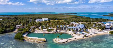 An aerial view of a coastal resort with multiple buildings, a beach, and clear turquoise waters.