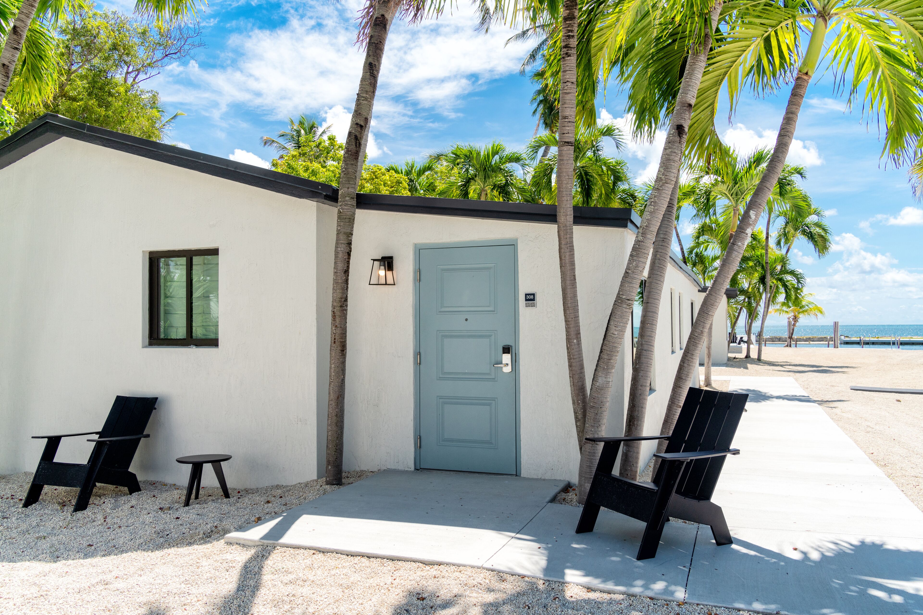A beachfront building with a light blue door, two black chairs, and a small table.