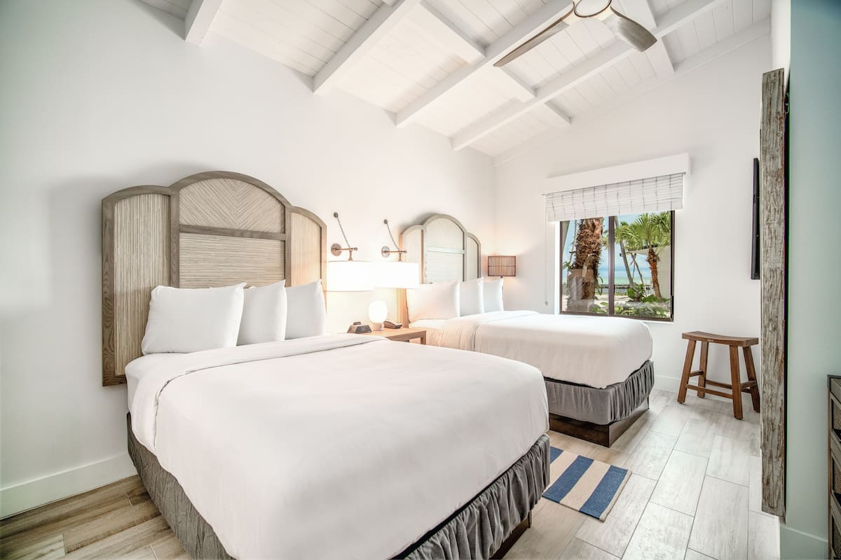A hotel room with two beds, a large window with a view, and a ceiling with exposed beams.