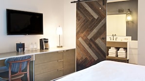 A modern hotel room with a flat-screen TV, a desk with a lamp, a chair, a bed, a sliding shower curtain, a vanity with a mirror, and a towel rack. - Hotel Becket, BW Signature Collection (South Lake Tahoe)