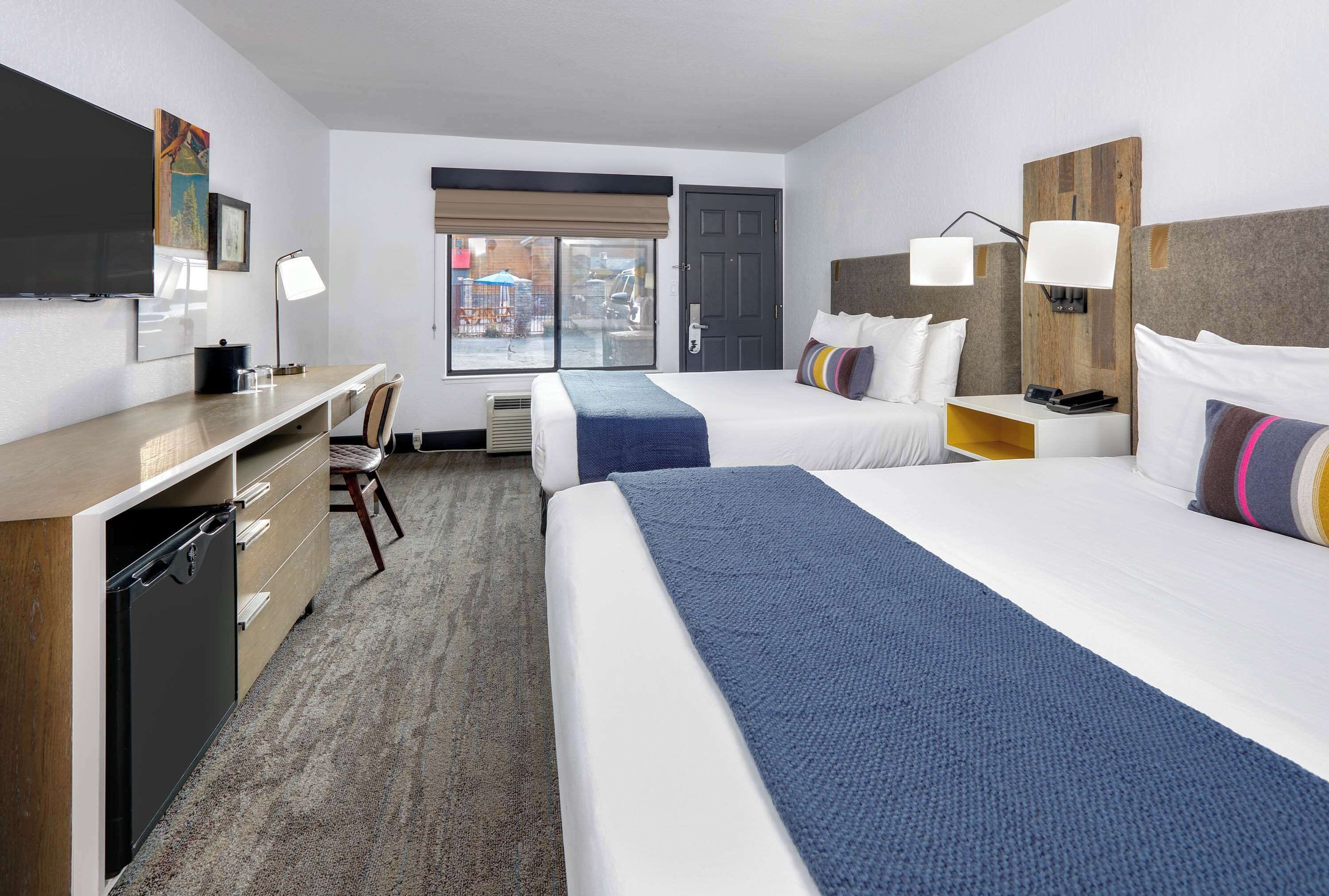 Hotelkamer met twee bedden, een bureau, een stoel, een televisie en een raam met uitzicht op de straat.
