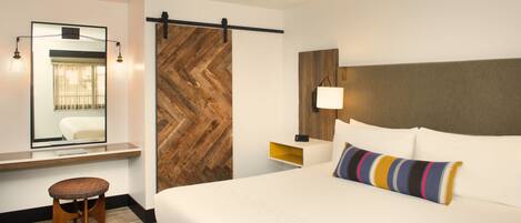 Habitación de hotel con una cama grande, un revestimiento de madera con patrón de espiga, un escritorio con silla y un espejo.