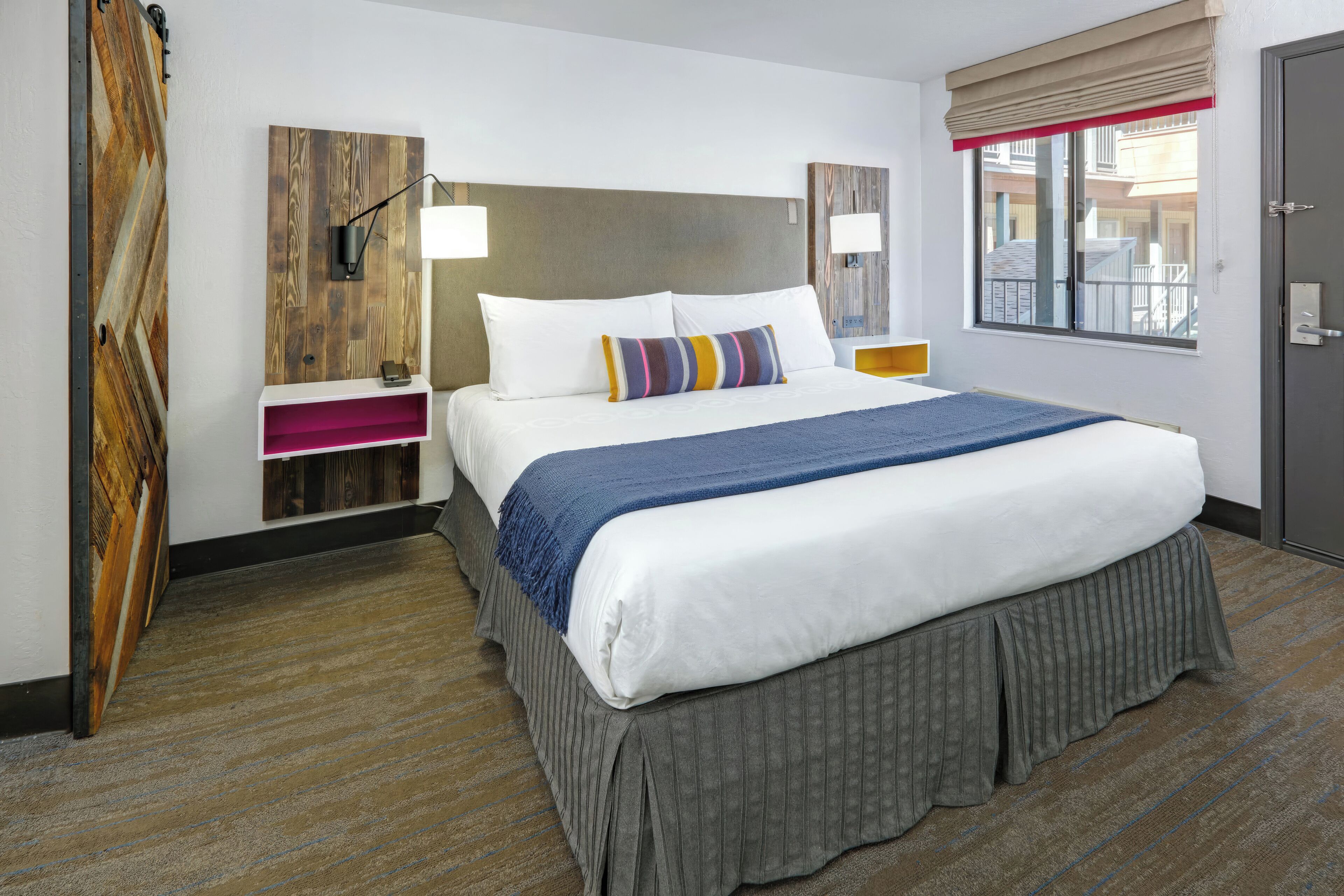 A hotel room with a large bed, a wooden headboard, a window with a view, and a door.