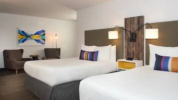 A hotel room with two beds, a desk, a chair, a lamp, and a painting on the wall.