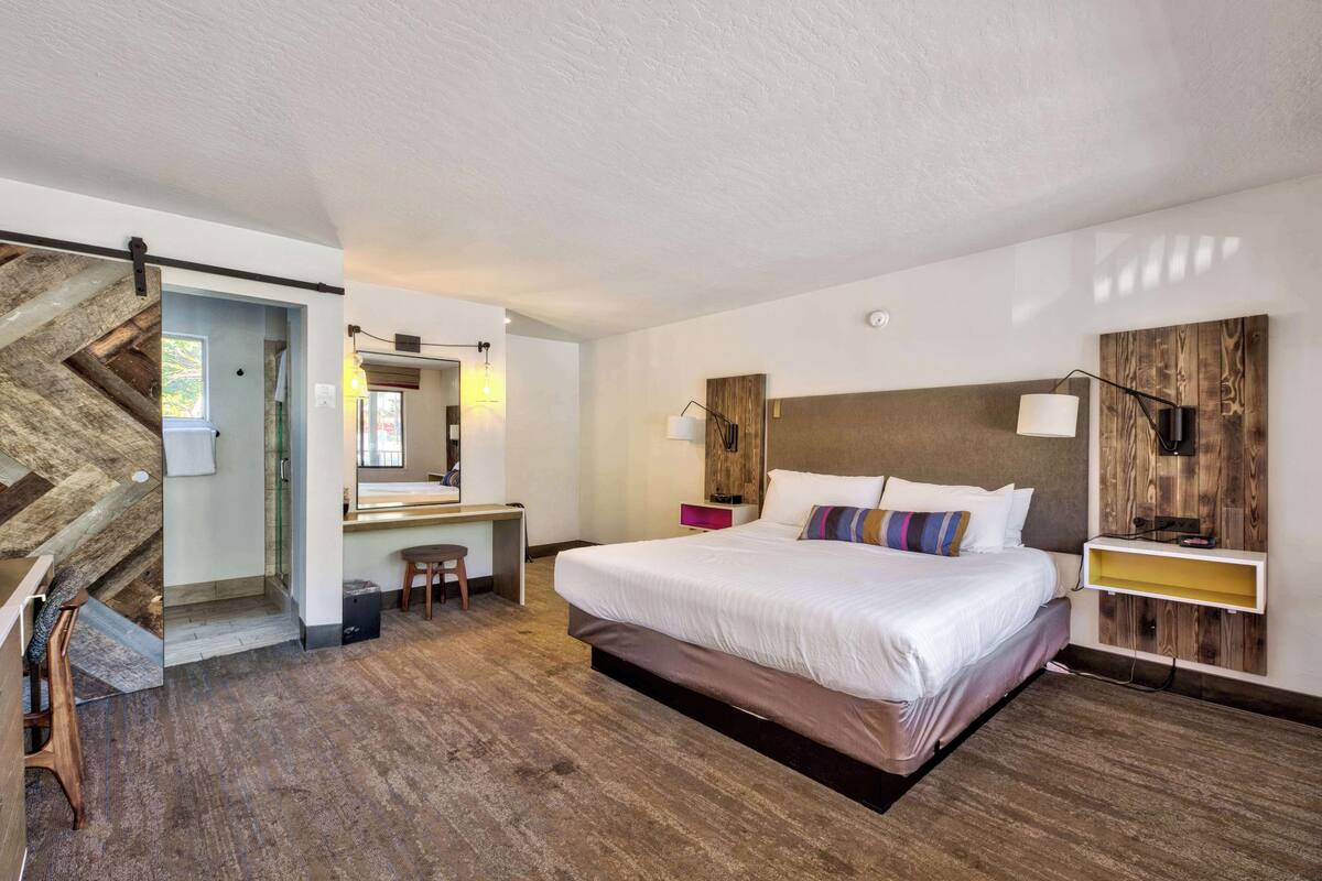 A modern hotel room with a large bed, a desk, and a mirror.