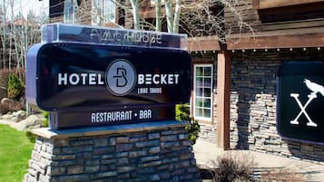 Ein Hotelschild mit rustikalem Aussehen, einem steinernen Sockel und einem Logo, das einen Restaurant- und Barbereich signalisiert.