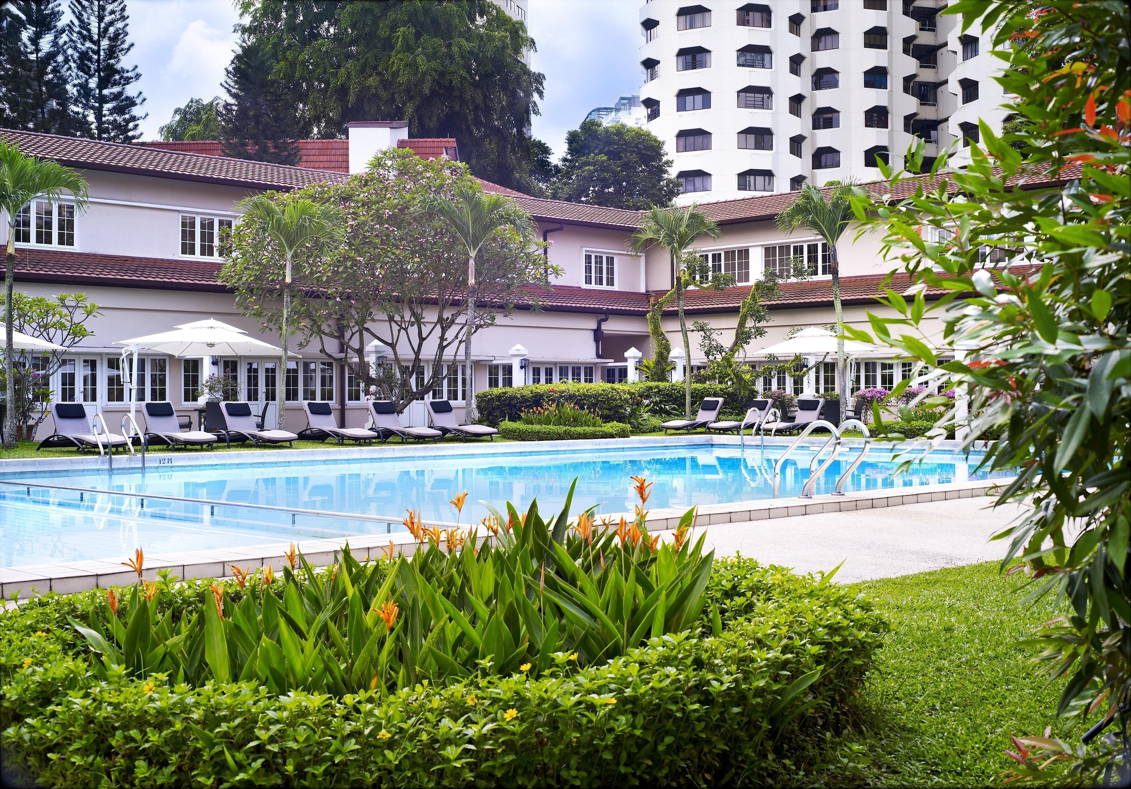 Un hotel con piscina, sillas de descanso y un edificio con varios balcones.
