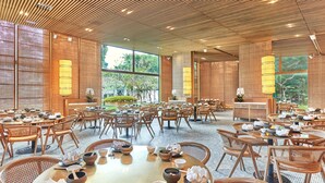 A spacious dining area with multiple tables and chairs, large windows, and a wooden ceiling. - Goodwood Park Hotel (Singapore)