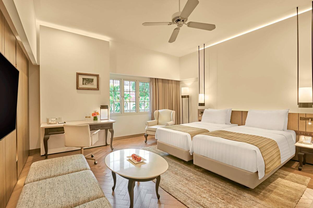 Habitación de hotel con dos camas, un escritorio, una silla, un televisor y un ventilador de techo.