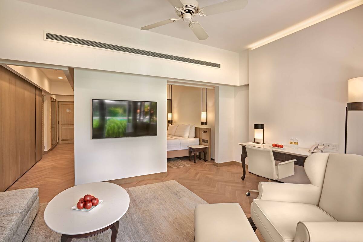 Una habitación de hotel moderna con televisión de pantalla plana, un escritorio con lámpara, un sofá y una silla.