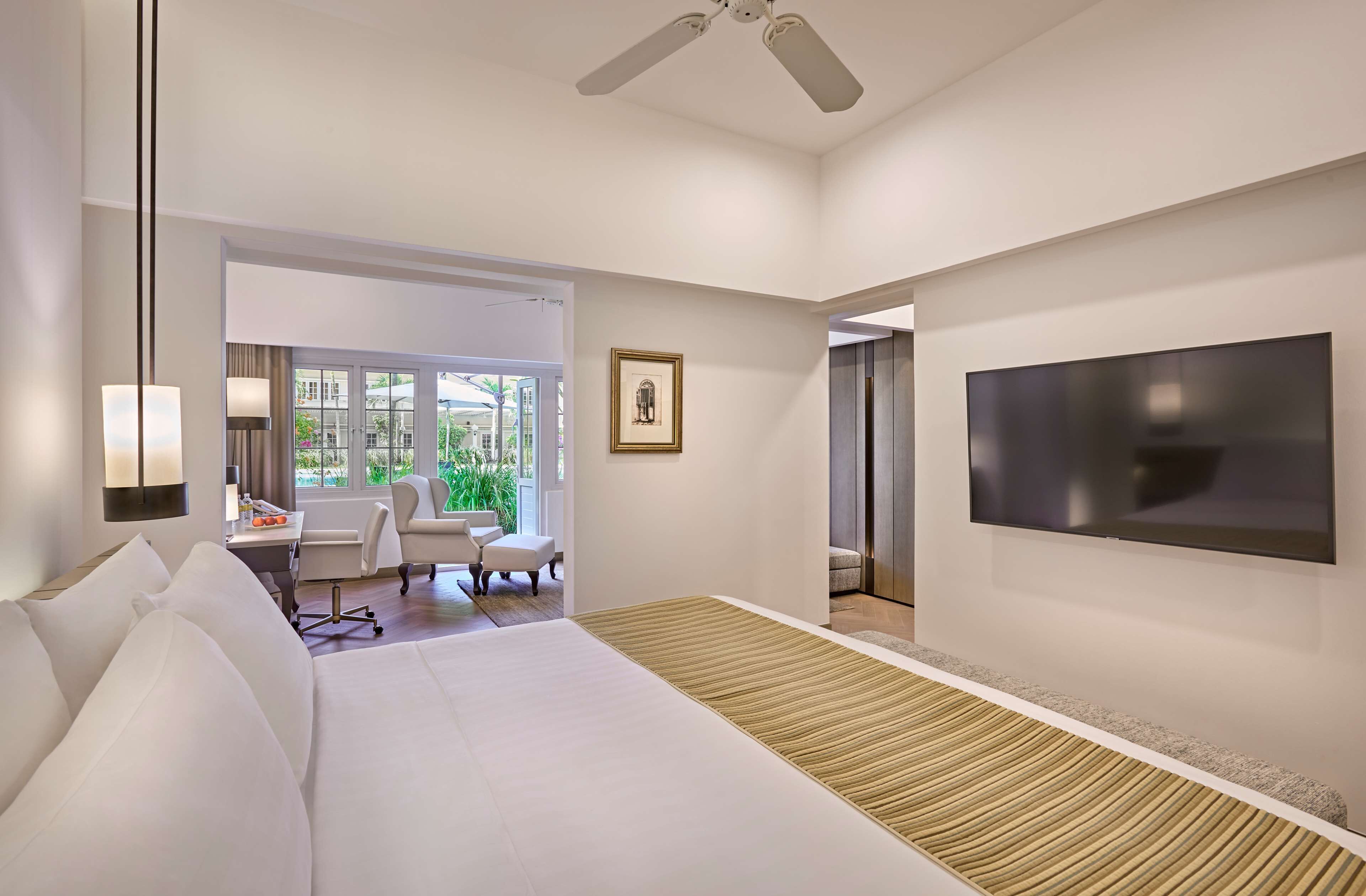 Una habitación de hotel moderna con una cama grande, un escritorio con una silla, un televisor y una ventana con vistas a zonas verdes.